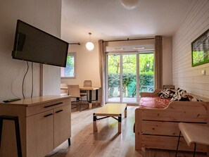 A modern living room with a flat-screen TV, wooden furniture, a dining area, and a sliding glass door leading to a garden. - Apartment with a terrace and an outdoor pool (Ax-les-Thermes)