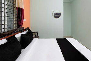 Habitació d'hotel amb un llit, una finestra amb persianes, un termòstat fixat a la paret i un mirall rodó petit.