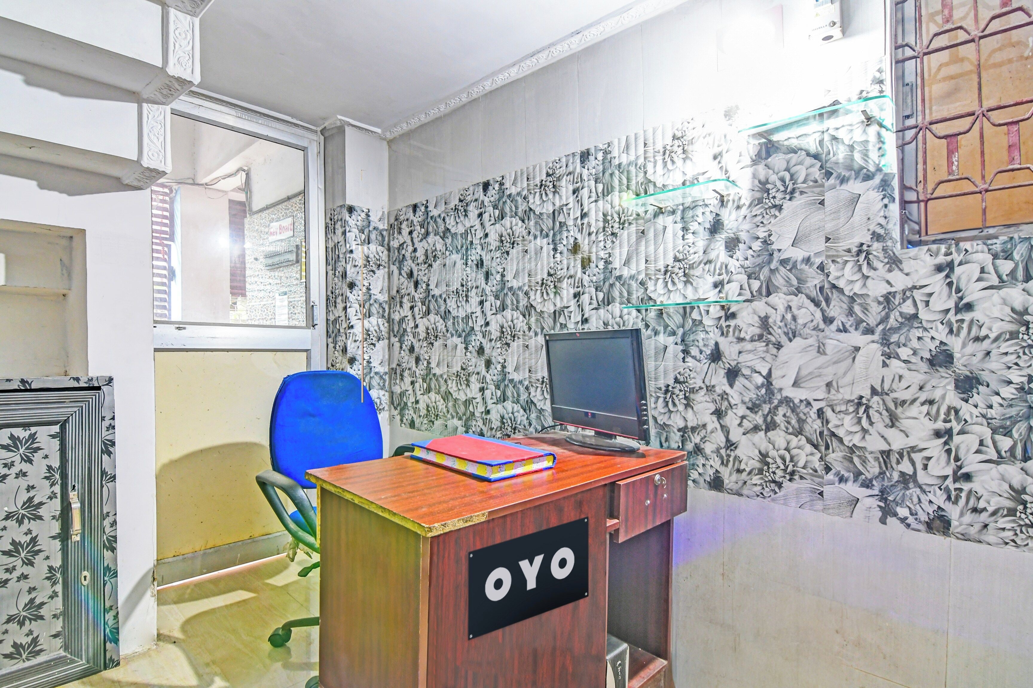 Una habitación con escritorio, una silla, computadora y una pared con estampado floral.