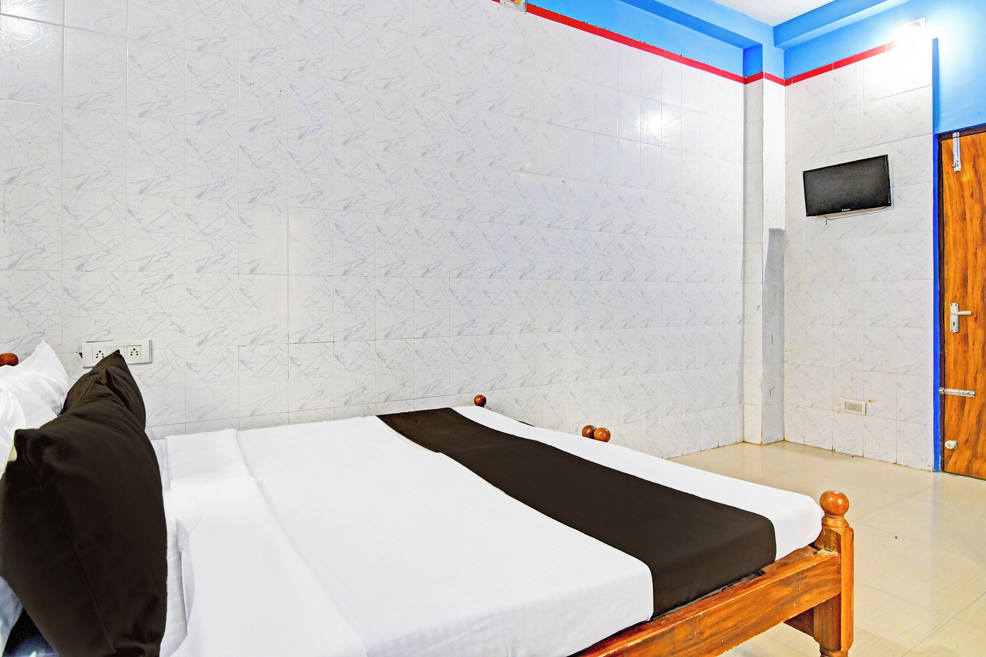 A hotel room with a bed, a wooden door, and a wall-mounted TV.