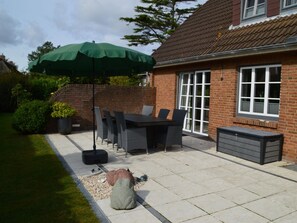 A patio with a table and chairs, a green umbrella, and a brick house. - Holiday Home in Nieblum With Swimming Pool (Nieblum)
