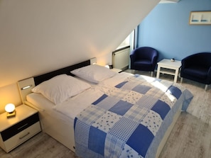 A bedroom with a bed, two chairs, a small table, and a nightstand with a lamp. - Holiday Home in Nieblum With Swimming Pool (Nieblum)