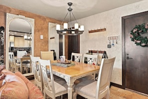 A dining area with a wooden table, white chairs, and a chandelier. - Ski In/Ski Out Access to Giant Steps (Brian Head)