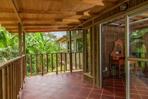 A wooden balcony with a tiled floor, surrounded by lush greenery. - LA CABAÑA EN The GUADUAL (San Antonio Del Tequendama)