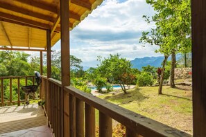 A wooden deck with a barbecue grill, overlooking a landscaped area with a pool and trees. - LA CABAÑA EN The GUADUAL (San Antonio Del Tequendama)