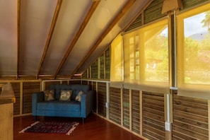 A room with a sloped ceiling, wooden beams, a blue sofa, and large windows. - LA CABAÑA EN The GUADUAL (San Antonio Del Tequendama)