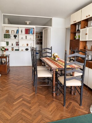Un coin repas avec un parquet en chevrons, une table recouverte d’une nappe à motifs et des chaises dotées d’assises rembourrées.