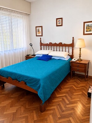A neatly made bed with a blue bedspread, a wooden headboard, and a bedside lamp on a wooden nightstand. - New Listing (Montevideo)
