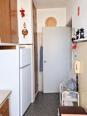 A compact kitchen with a white refrigerator, a clock on the wall, and a door with a striped towel hanging. - New Listing (Montevideo)