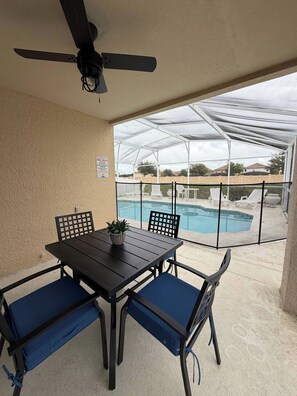 An outdoor patio with a table and chairs, a ceiling fan, and a view of a swimming pool through a covered area. - Cozy Home minutes from Disney (Davenport)