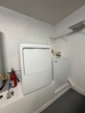 A laundry room with a white washing machine and dryer, a fire extinguisher, and a small shelf with items. - Cozy Home minutes from Disney (Davenport)