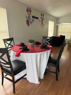 A dining area with a table set for four, black chairs, a red tablecloth, and a wall decal featuring cartoon characters. - Cozy Home minutes from Disney (Davenport)