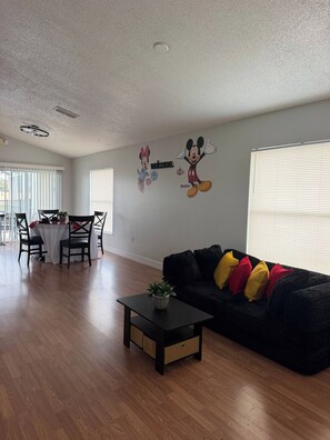 A living room with a black sofa, a small table with a plant, and a dining area with a table and chairs. - Cozy Home minutes from Disney (Davenport)