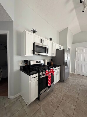 A kitchen with white cabinetry, a stainless steel refrigerator, a microwave, a stove, and a tiled floor. - Cozy Home minutes from Disney (Davenport)