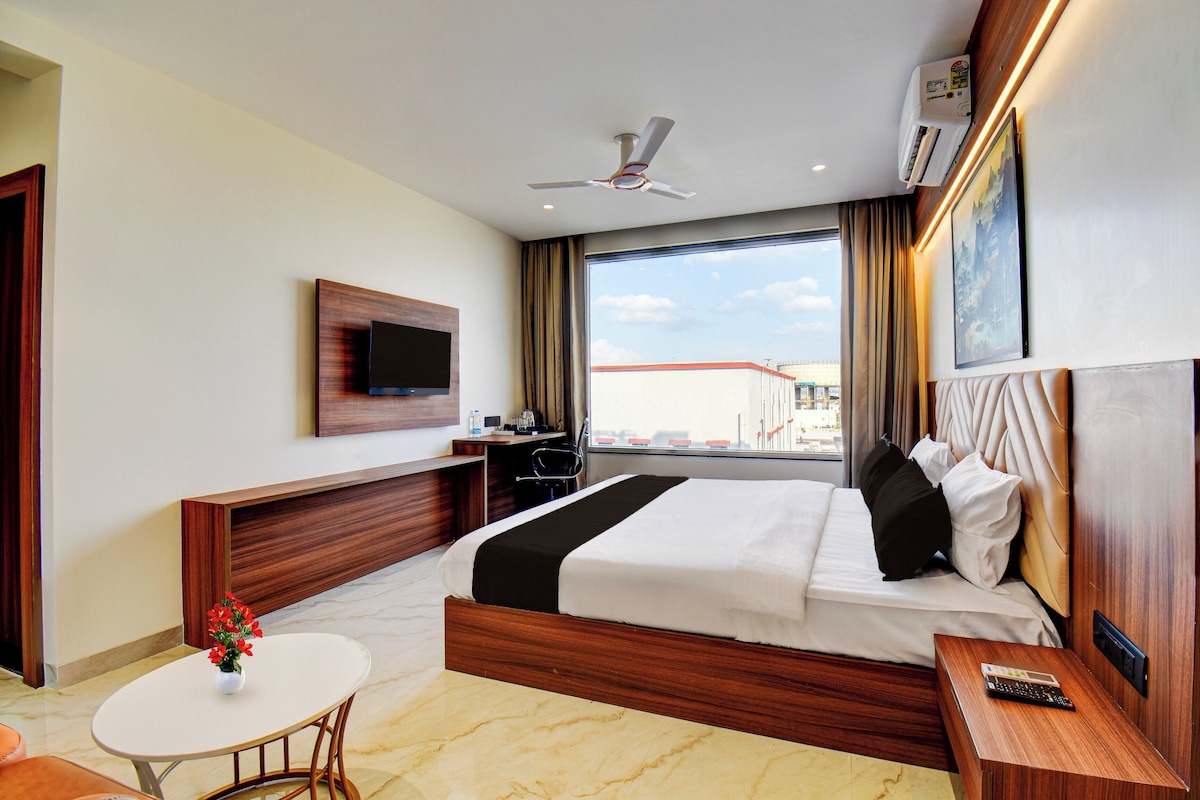 A hotel room with a bed, a desk, a TV mounted on the wall, a window with curtains, and a ceiling fan.