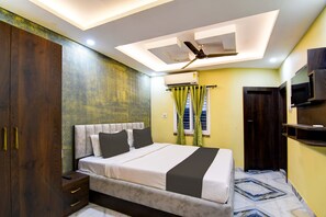 Une chambre à coucher comprenant un lit, une armoire, un ventilateur de plafond, un appareil de climatisation, un téléviseur et une fenêtre avec des rideaux.