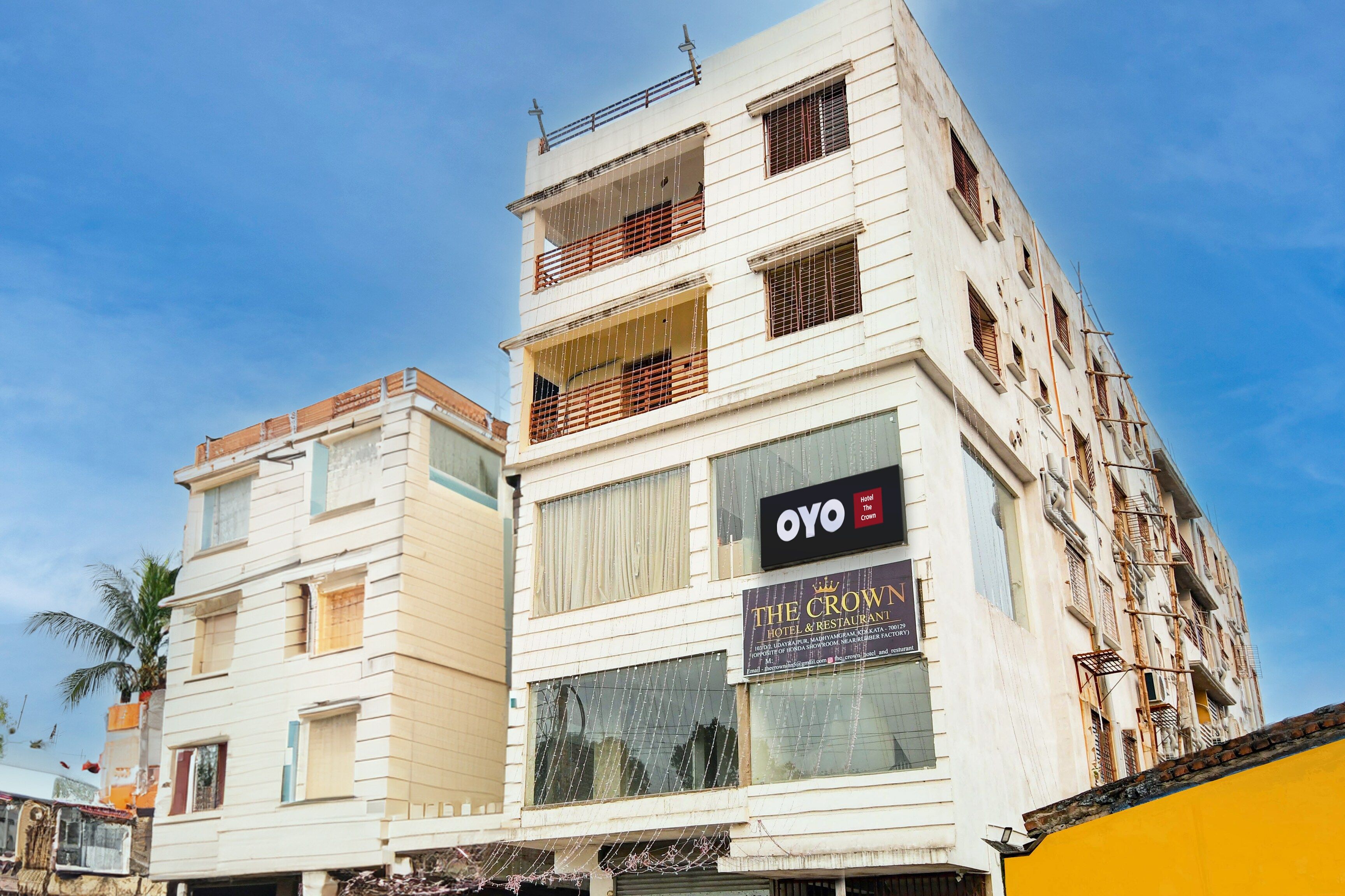 Um hotel de vários andares com varandas, um letreiro indicando 'OYO Hotel & Restaurant' e uma placa com 'The Crown'.