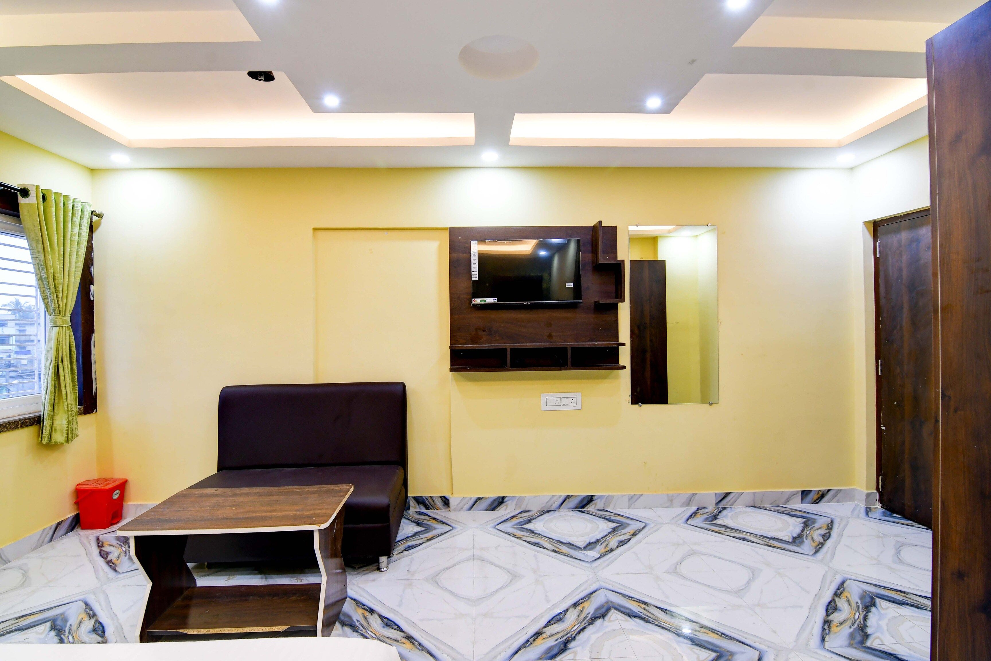 A room with a sofa, a TV mounted on the wall, a small table, and a patterned floor.