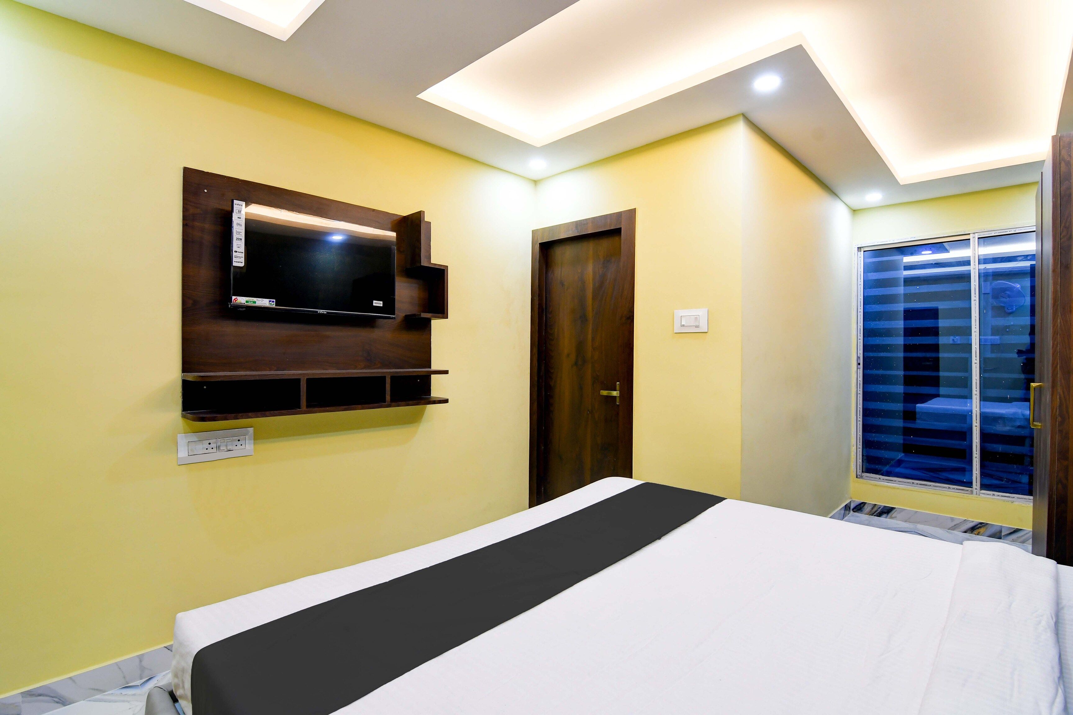 Un dormitorio con cama, televisor montado, puerta y ventana con persianas.