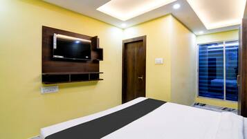 Un dormitorio con cama, televisor montado, puerta y ventana con persianas.