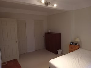 A bedroom with a bed, a dresser, a nightstand with a lamp, and two closed doors. - Cozy Roomy 2 Bedroom unit in Quiet area close to downtown, Parks, shops, transit (Ottawa)
