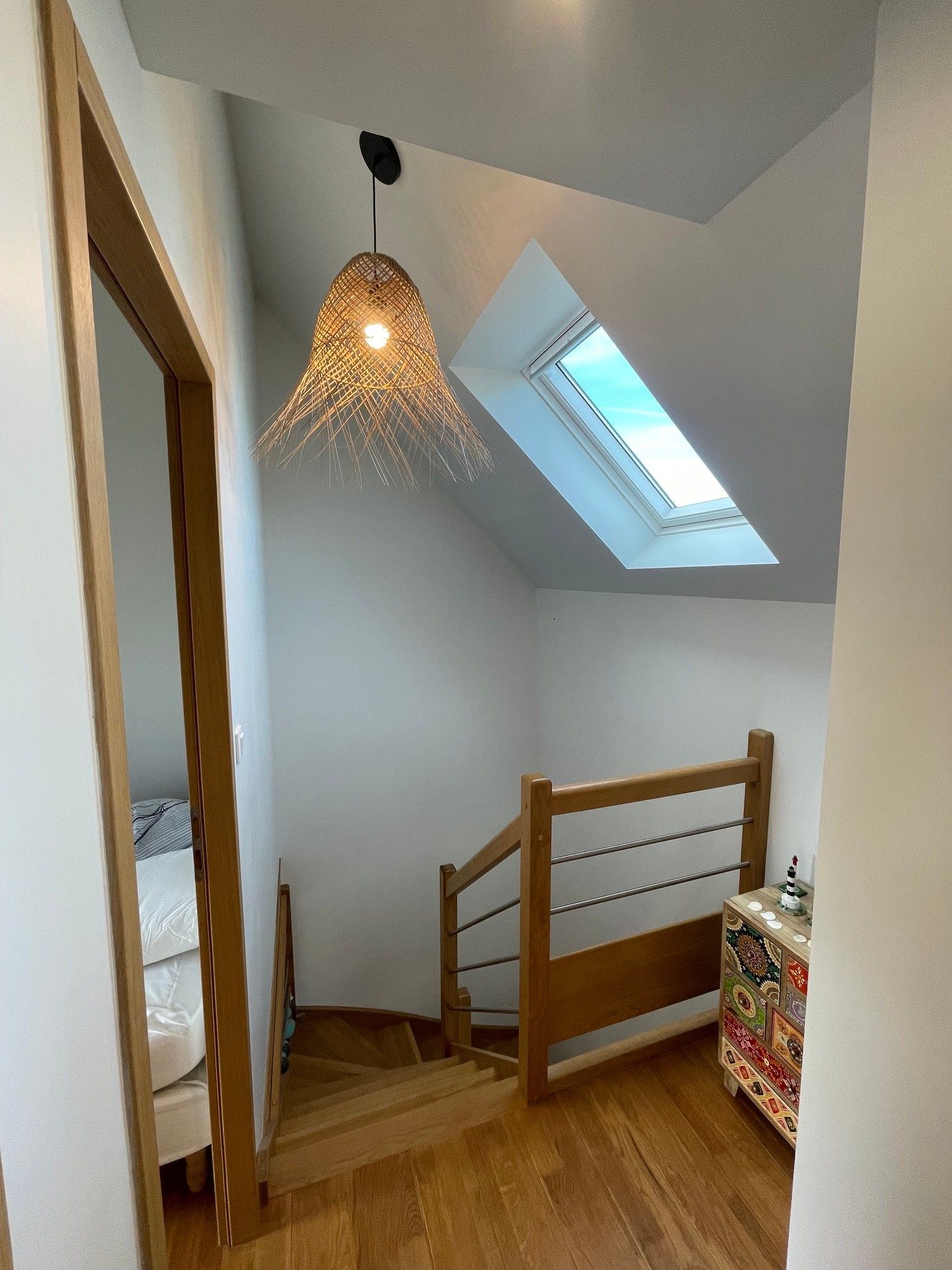 Ein Zimmer mit schrägen Wänden, einem Oberlicht, einer Holztreppe und einem Bett.