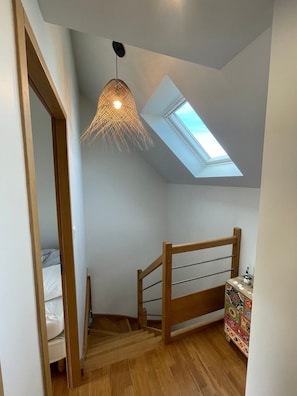 A room with a sloped ceiling, a skylight, a wooden staircase, and a bed.