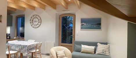 A cozy loft bedroom with a dining area, a large window with a view, and a rustic wooden ceiling.