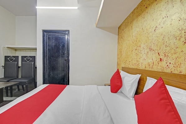 A hotel room with a bed, a wooden headboard, a door, and a table with chairs.
