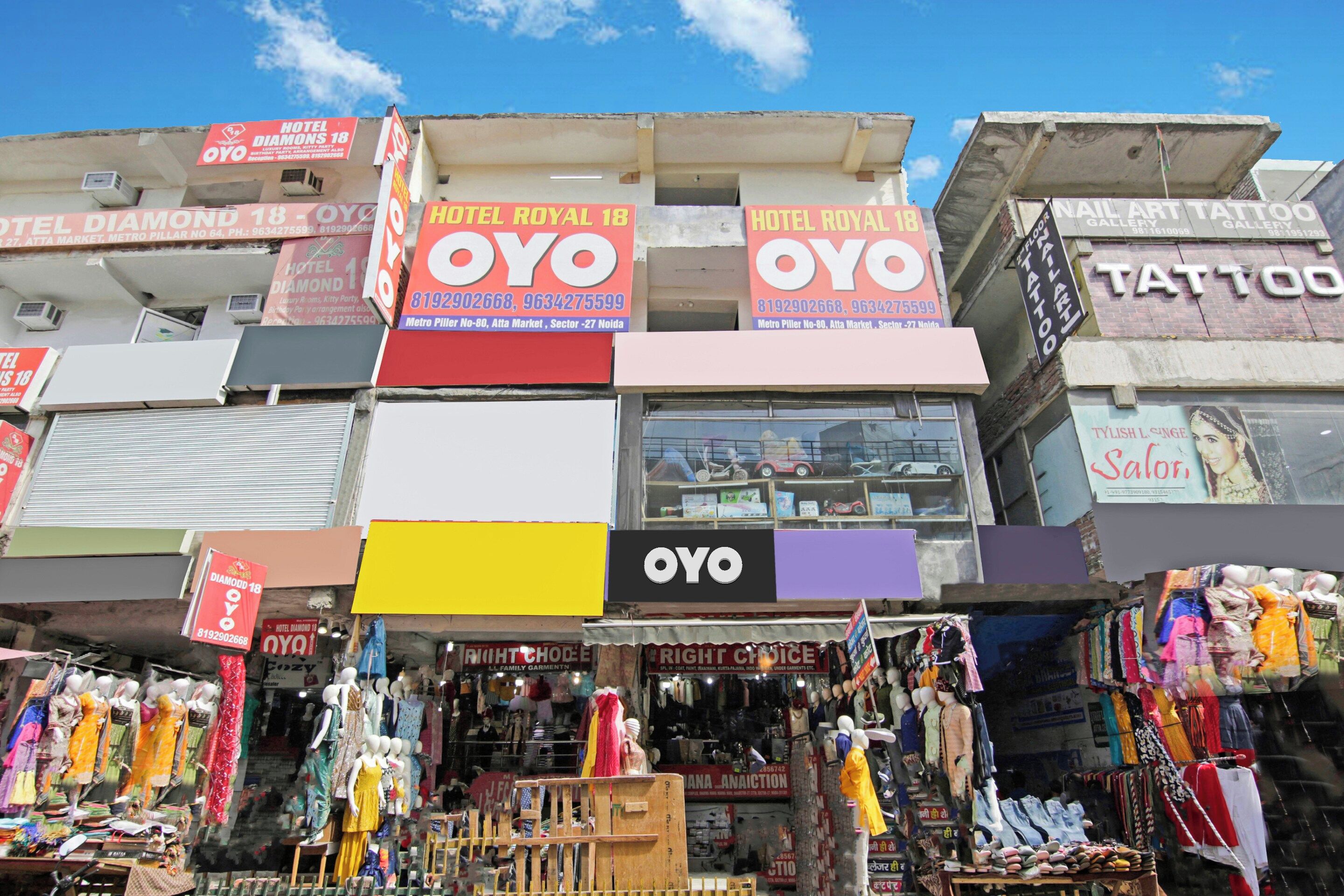Un edificio de varios pisos con letreros que indican Hotel Royal 18 y OYO, y un escaparate visible con maniquíes exhibiendo ropa.