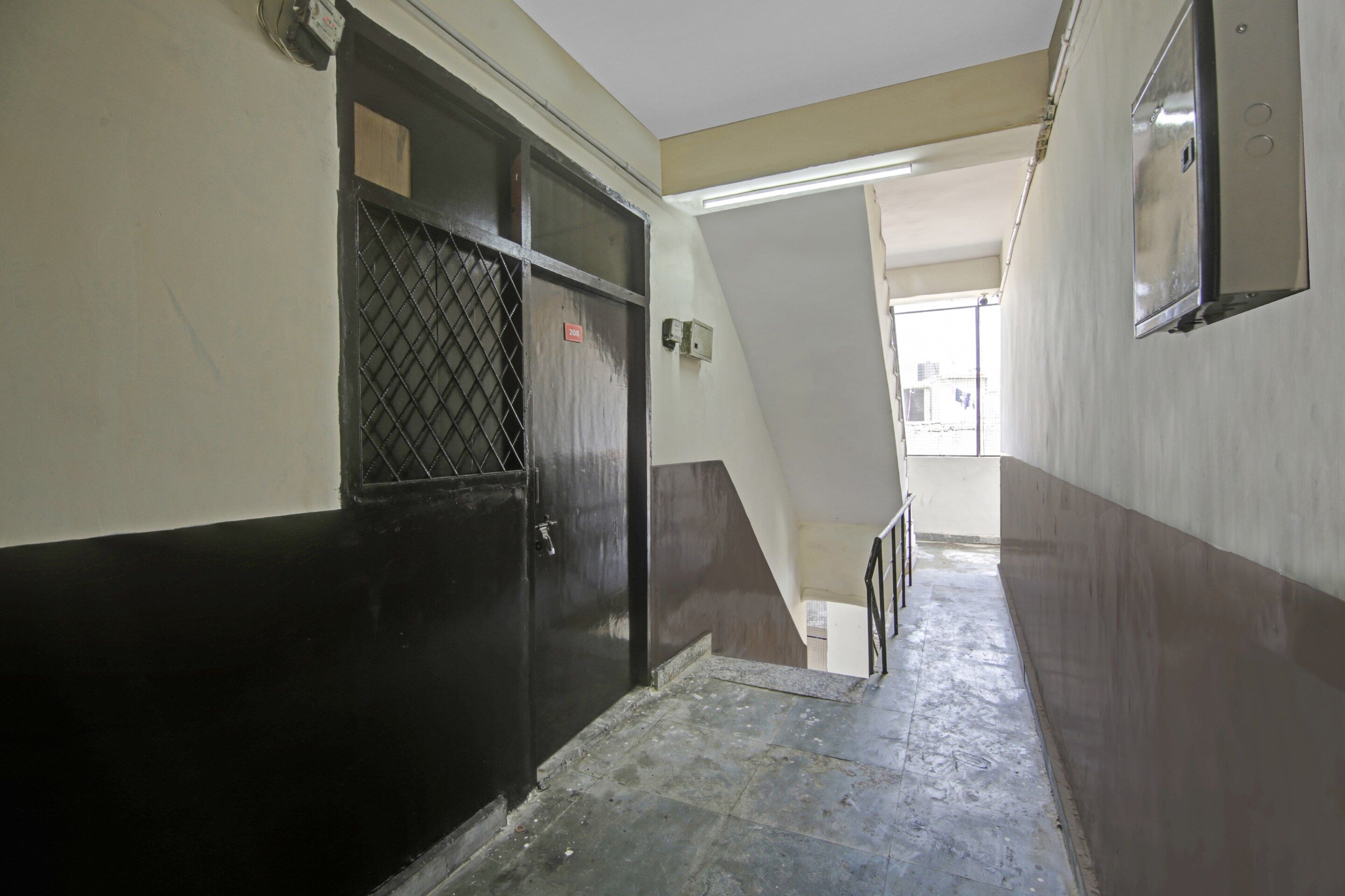 Un pasillo estrecho con una puerta a la izquierda, una escalera a la derecha y una lámpara arriba.