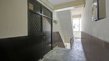 Un pasillo estrecho con una puerta a la izquierda, una escalera a la derecha y una lámpara arriba.