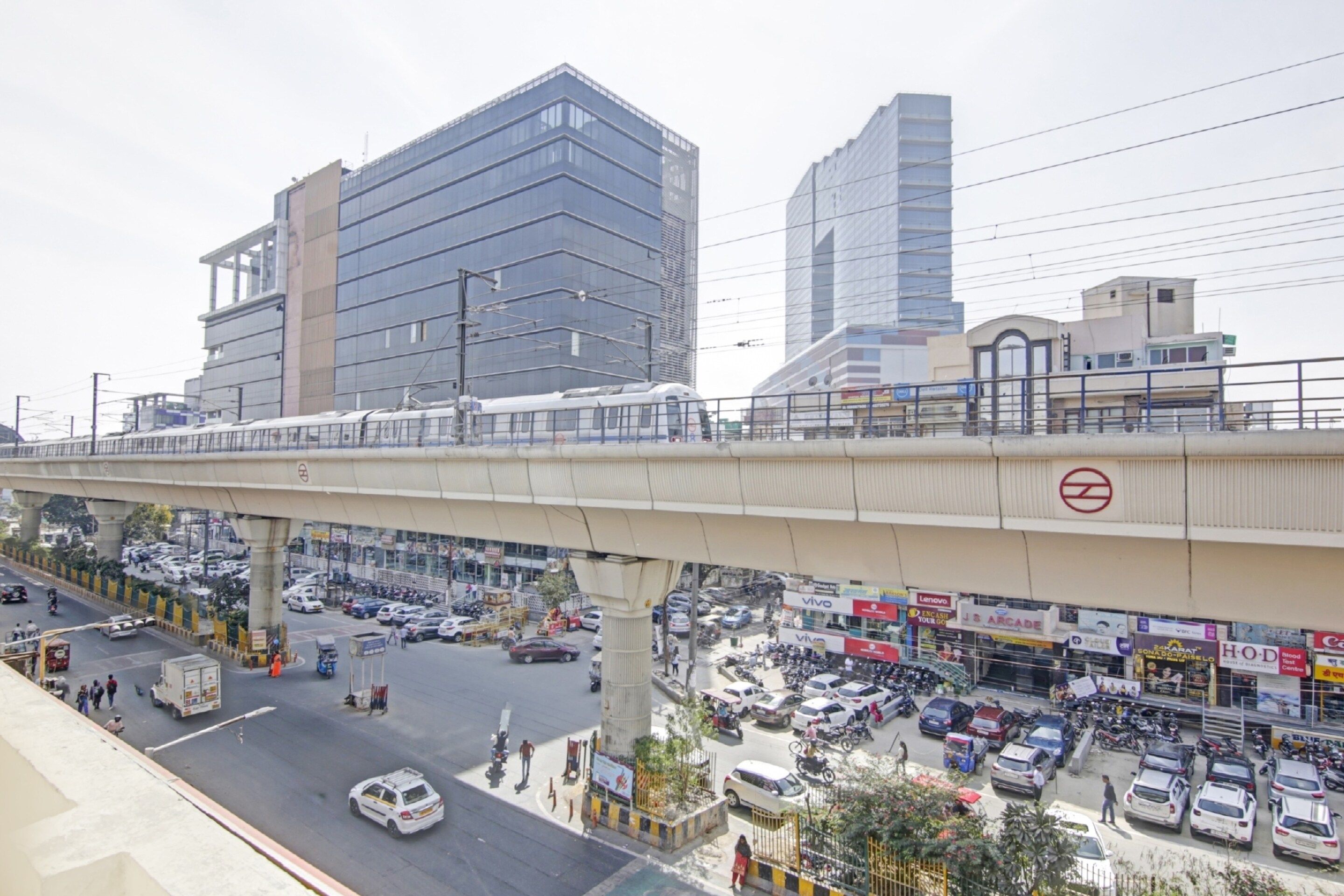 Una concurrida calle urbana con un puente peatonal, edificios comerciales y diversos vehículos.