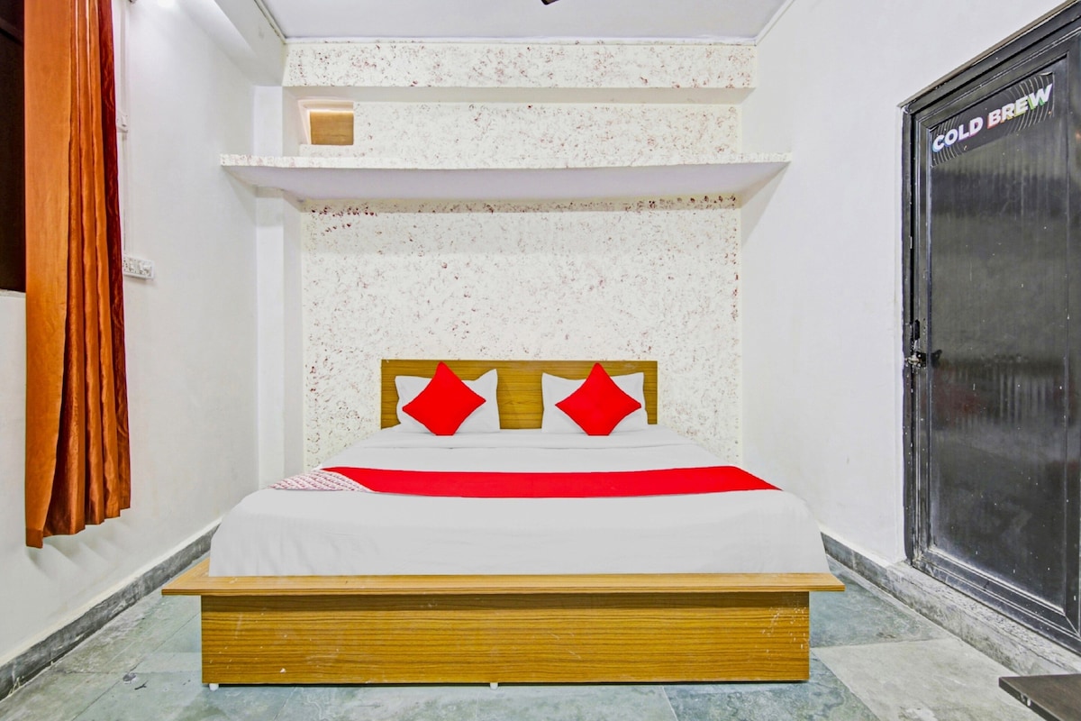 A bedroom with a bed, a wooden headboard, a red pillow, and a door labeled 'COLD BREW'.