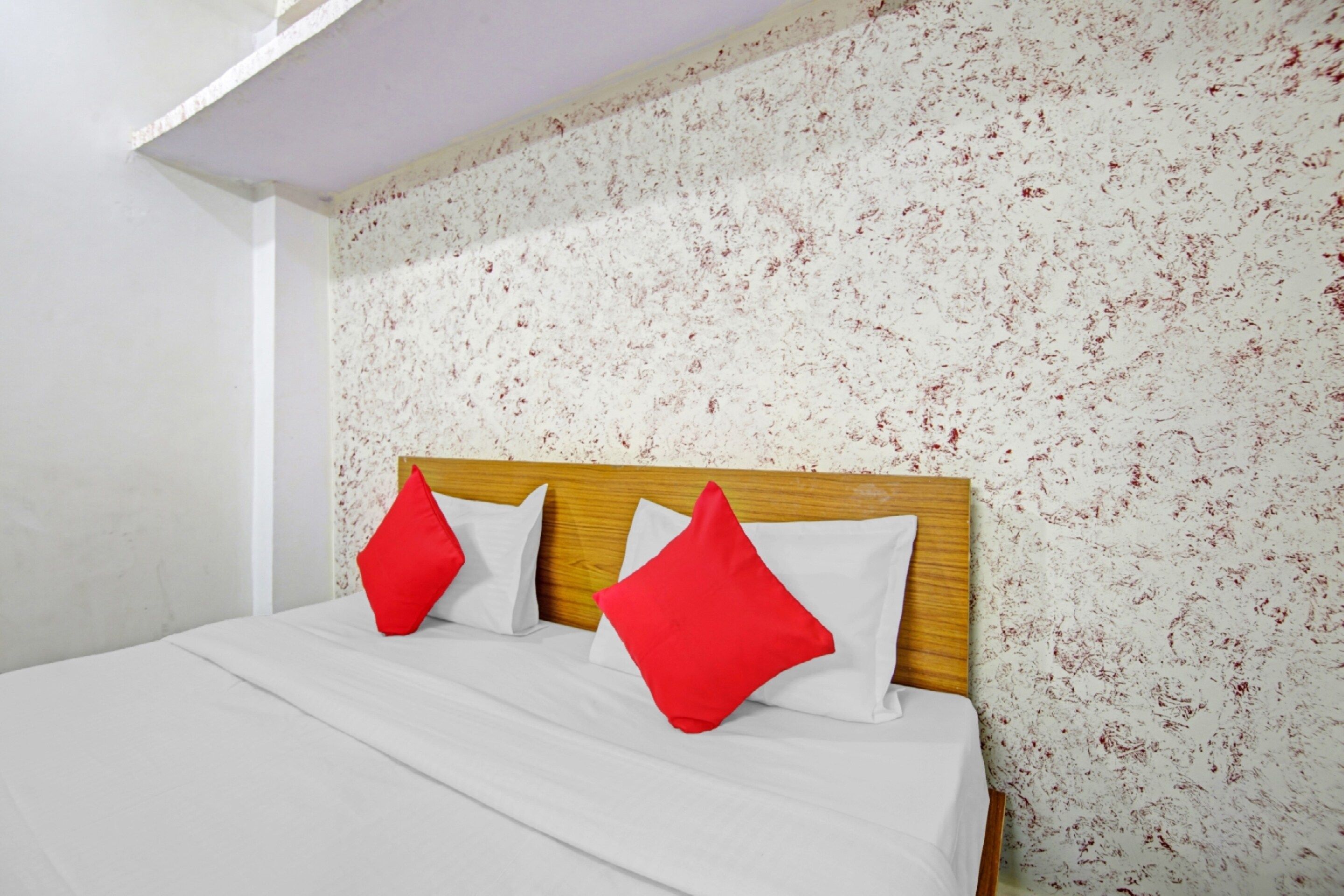 Ein Bett mit weißer Bettwäsche und zwei roten Kissen, ein hölzernes Kopfende und eine Wand mit einem Blumenmuster.