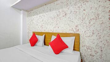Ein Bett mit weißer Bettwäsche und zwei roten Kissen, ein hölzernes Kopfende und eine Wand mit einem Blumenmuster.