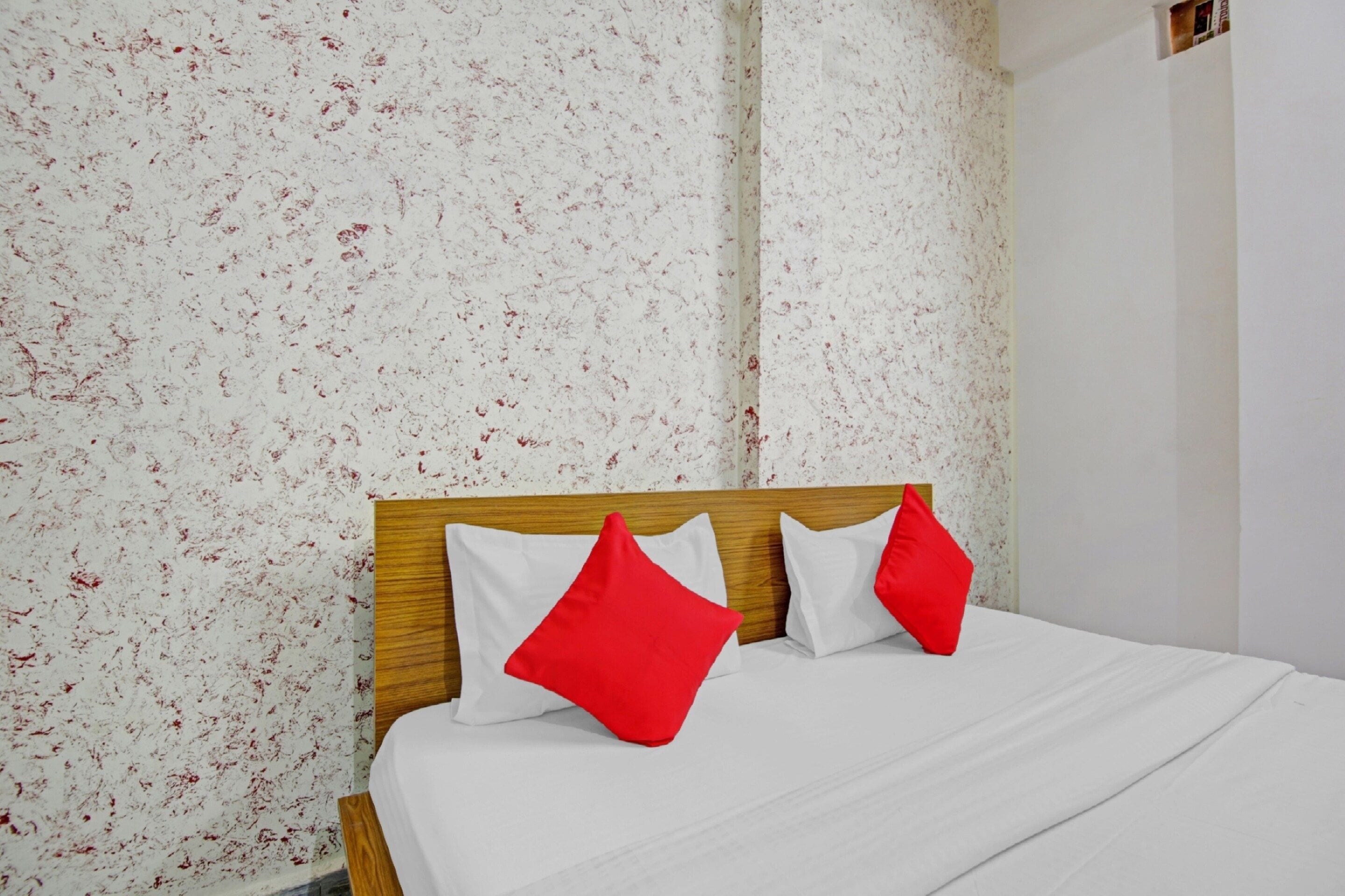 Una cama con cabecera de madera, ropa de cama blanca y dos almohadas rojas.