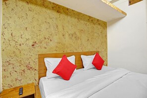 A hotel room with a wooden headboard, white bedding, and red pillows.
