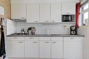 A kitchen with white cabinets, a gas stove, a kettle, a coffee maker, and a microwave. - New Listing (Grou)
