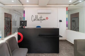 A reception desk with a black counter, a wall-mounted air conditioner, and a glass partition with a decorative design. - Collection O PRANJUL INN (Prayagraj)