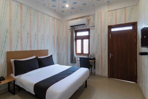 Habitación de hotel con cama, escritorio, silla, ventana con barrotes y puerta.
