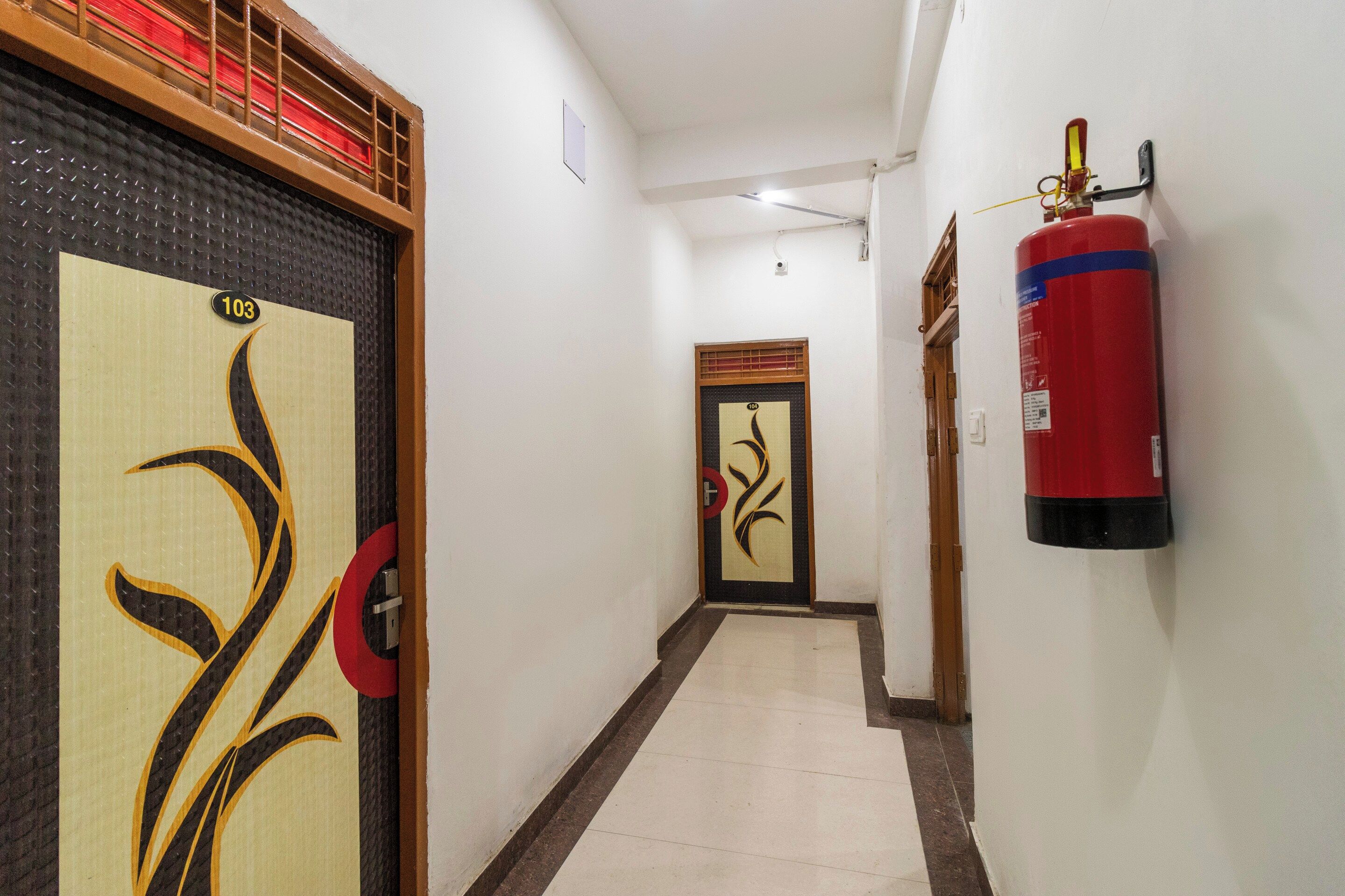 Un pasillo con un extintor montado en la pared, una puerta con un diseño decorativo y un cartel con el número 103 en la puerta.