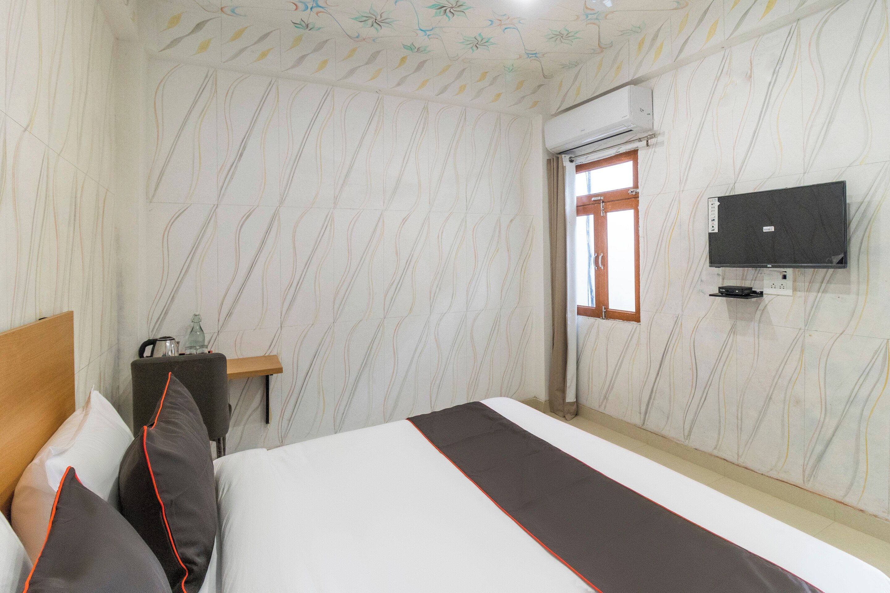 Habitación de hotel con cama, televisión instalada en la pared y ventana con cortinas.