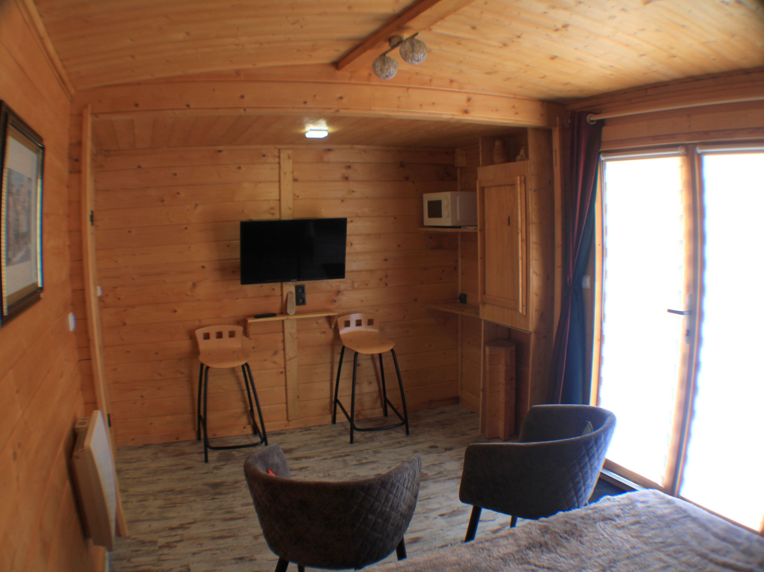Un intérieur en bois avec un téléviseur, deux tabourets de bar et un canapé.