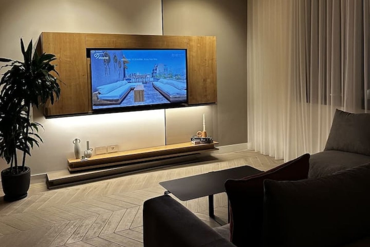 Ett modernt vardagsrum med en platt-TV som är monterad på en träpanel, en soffa, ett soffbord och en krukväxt.