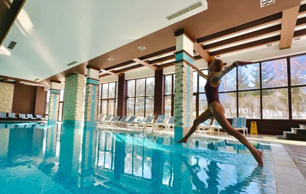 A swimming pool with clear water, surrounded by lounge chairs and a view of trees outside.