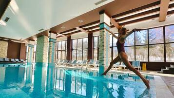 A swimming pool with clear water, surrounded by lounge chairs and a view of trees outside.