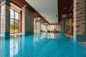 An indoor swimming pool with stone walls and large windows. - Hotel Terra (Razlog)