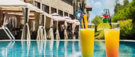 A swimming pool with two glasses of fruit juice, one with a heart-shaped straw and the other with a straw with a fruit decoration.