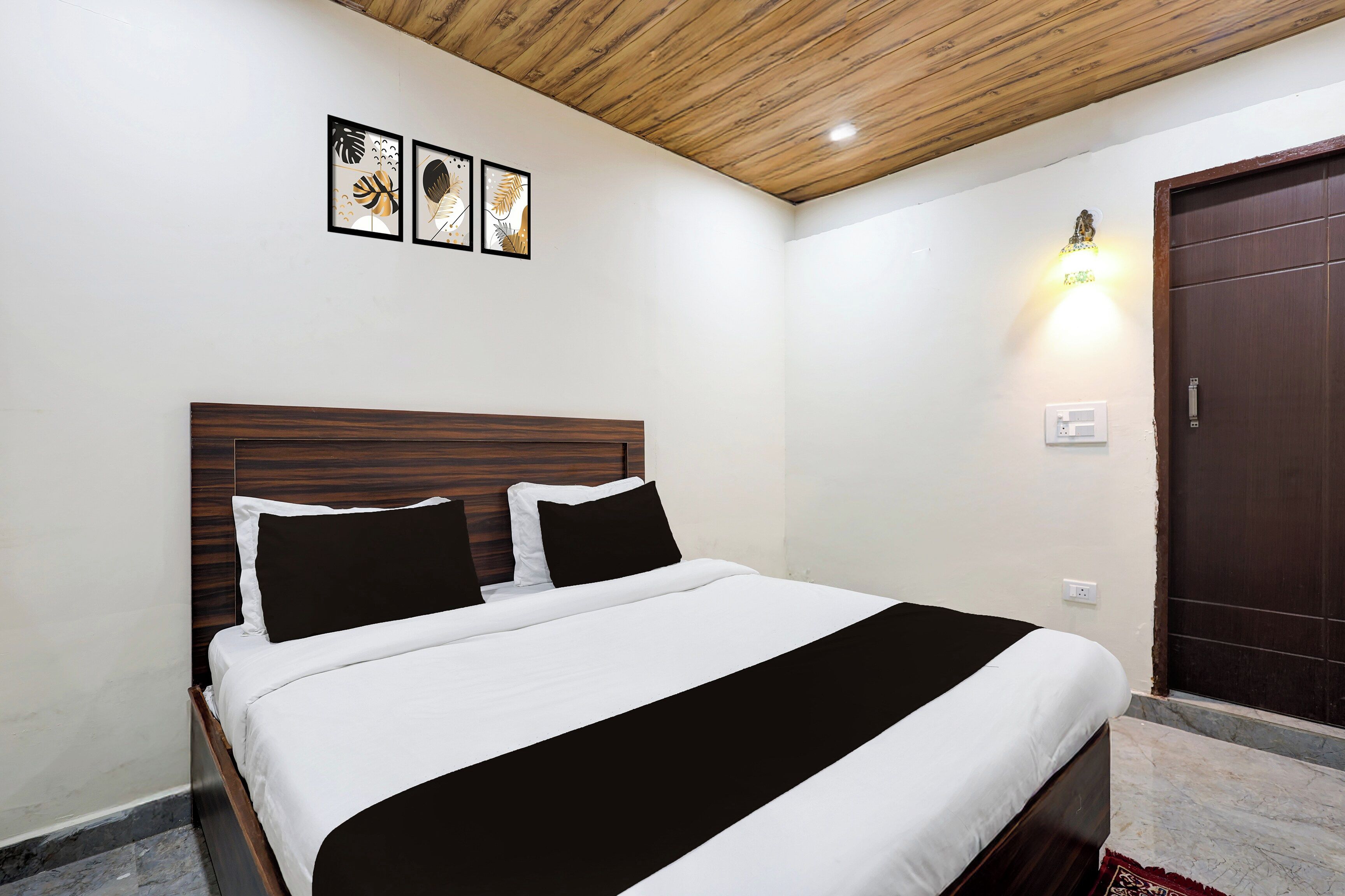 Ein ordentlich bezogenes Bett mit Holz-Kopfteil, einer Wandleuchte und einer Tür mit Griff.